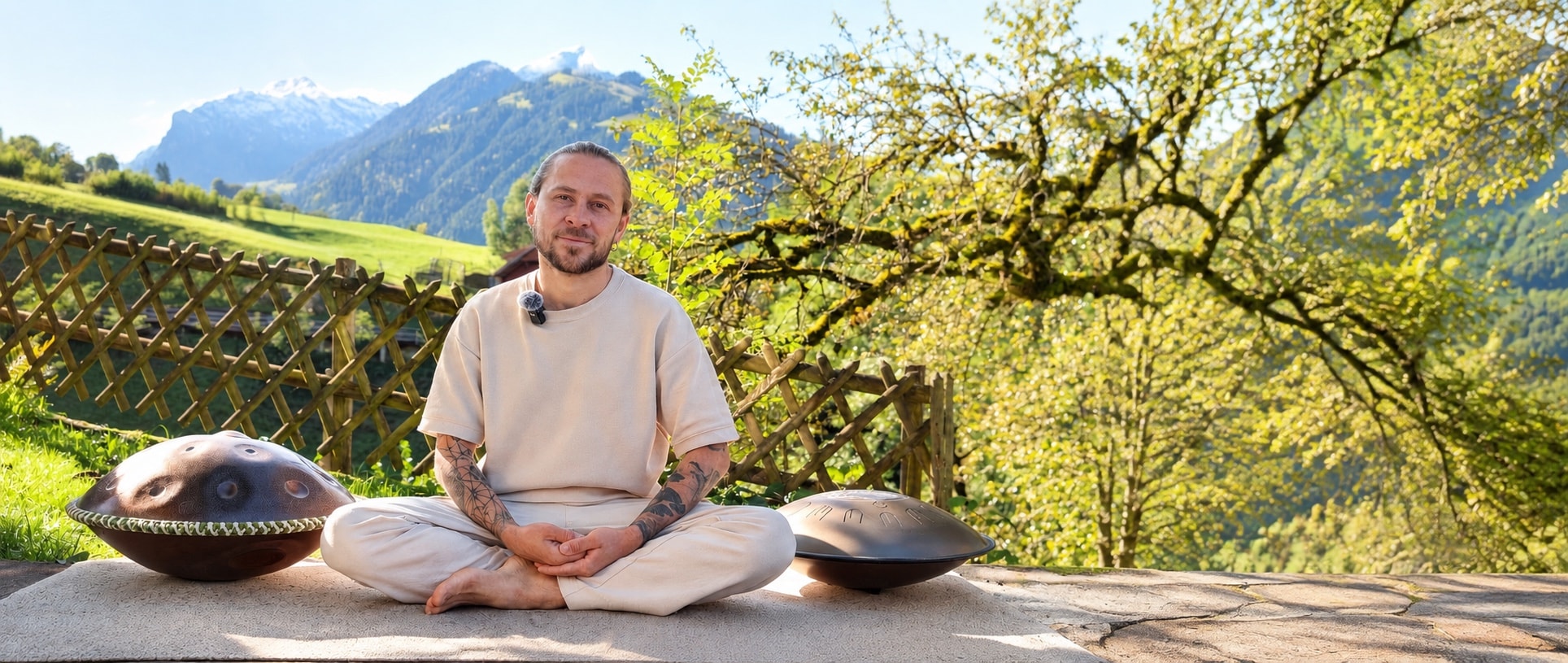 Denis sitting next to two handpans with mountains in the background