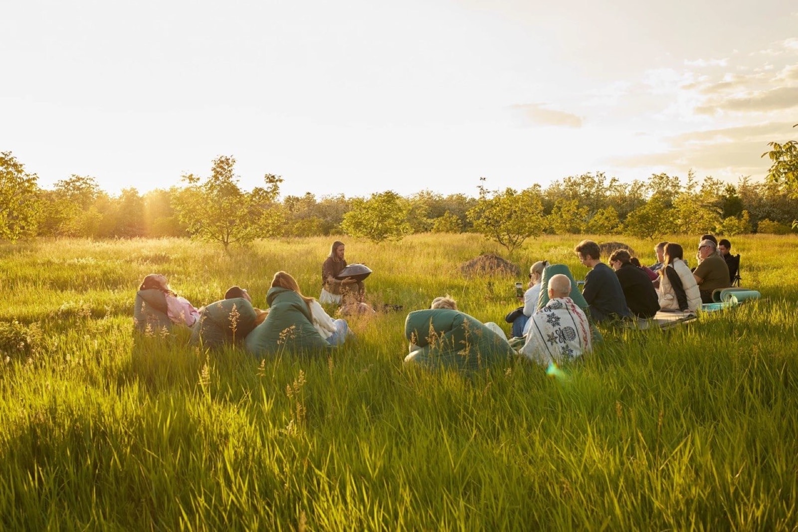 Denis playing handpan for a group of listeners in a field at sunset